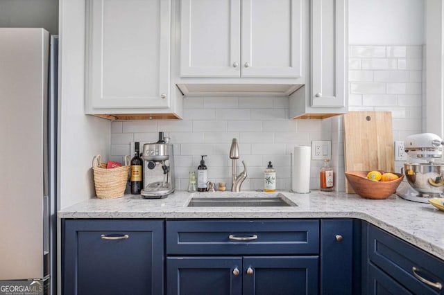 kitchen with blue cabinets, sink, stainless steel refrigerator, white cabinets, and backsplash