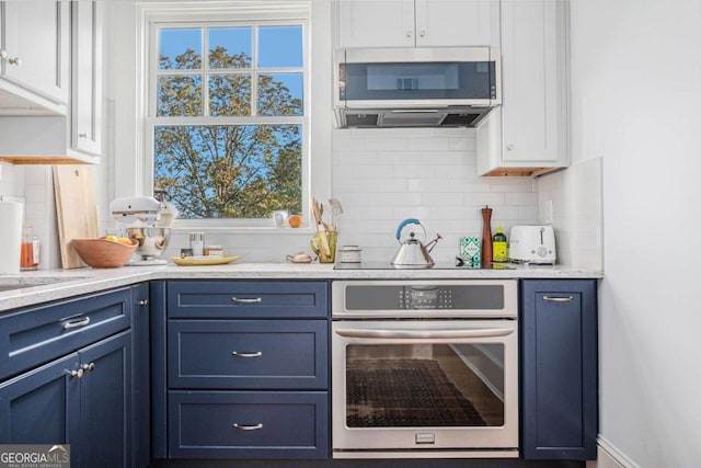 kitchen featuring blue cabinets, white cabinetry, oven, and backsplash