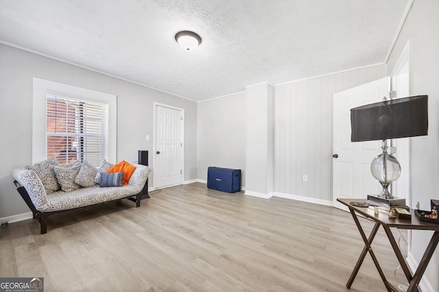 living area with crown molding, baseboards, light wood finished floors, and a textured ceiling