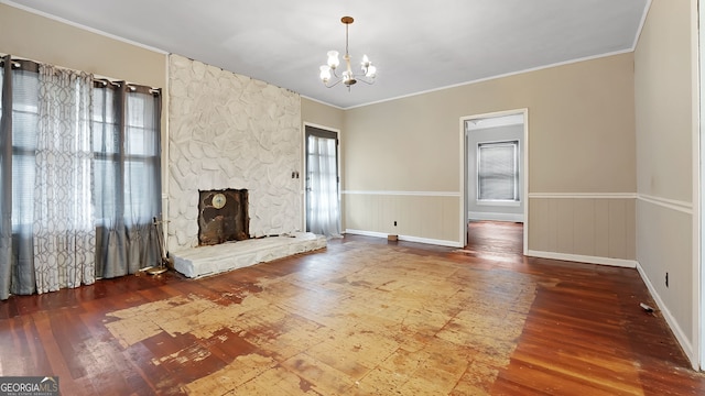 unfurnished living room featuring an inviting chandelier, ornamental molding, wood-type flooring, and a stone fireplace