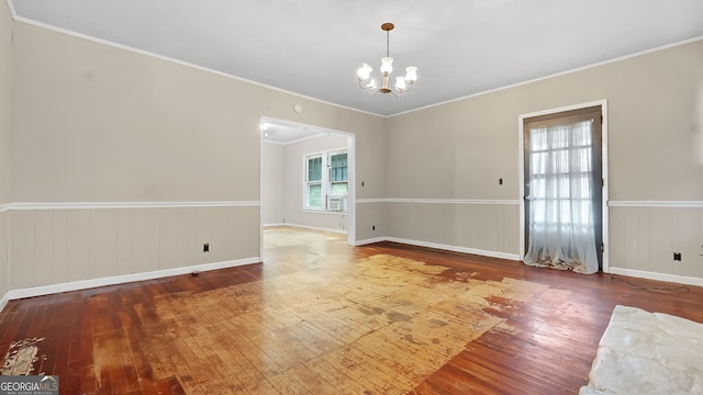 empty room with an inviting chandelier, hardwood / wood-style floors, and ornamental molding