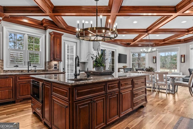 kitchen featuring dark stone countertops, hanging light fixtures, a center island, a chandelier, and light wood-type flooring