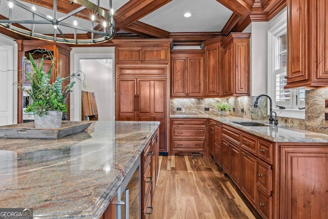 kitchen with light stone countertops, sink, hanging light fixtures, and light hardwood / wood-style flooring