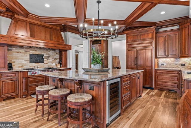 kitchen with a kitchen island, wine cooler, light stone counters, and decorative light fixtures