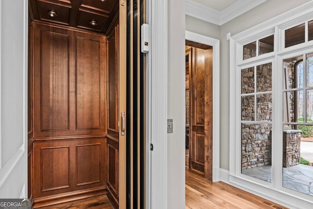 corridor featuring crown molding, elevator, and light wood-type flooring