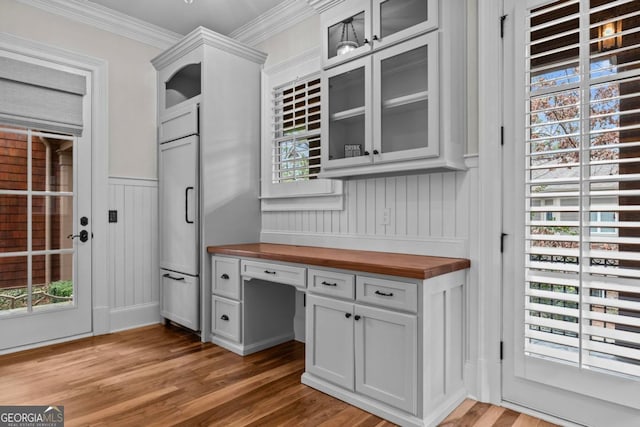 interior space featuring wood counters, white cabinetry, built in desk, light hardwood / wood-style flooring, and ornamental molding