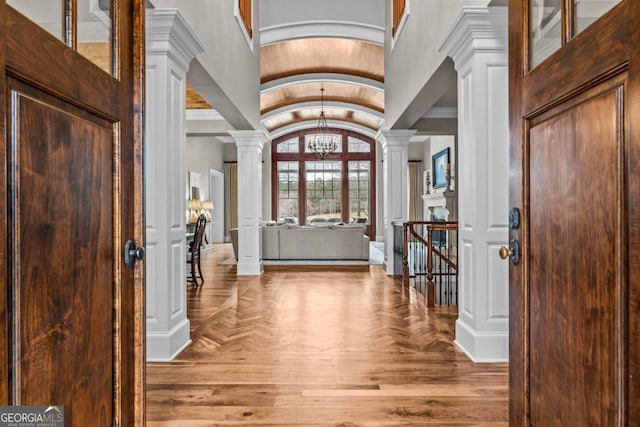 foyer entrance with decorative columns, wood-type flooring, lofted ceiling, and a notable chandelier