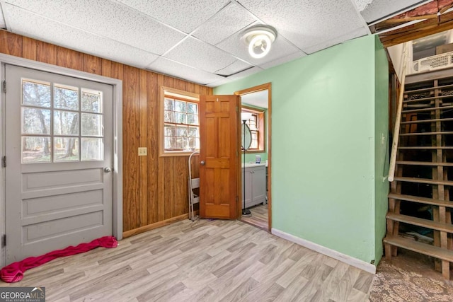 interior space with a paneled ceiling, light wood-type flooring, and wood walls