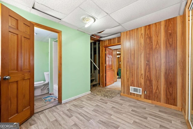 unfurnished room with a drop ceiling, light hardwood / wood-style flooring, and wood walls