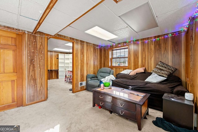 living room with light colored carpet, a paneled ceiling, and wood walls