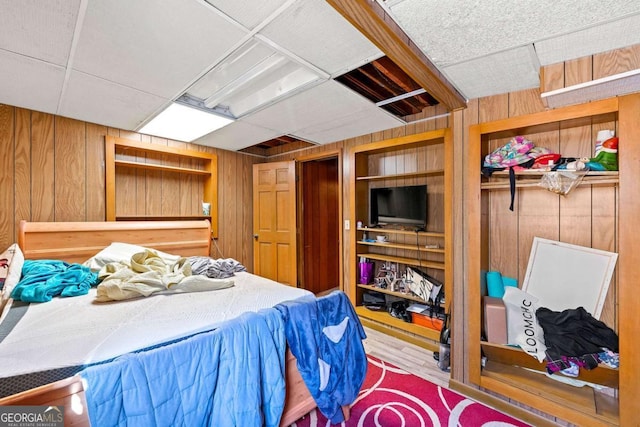 bedroom featuring a drop ceiling, hardwood / wood-style flooring, and wooden walls