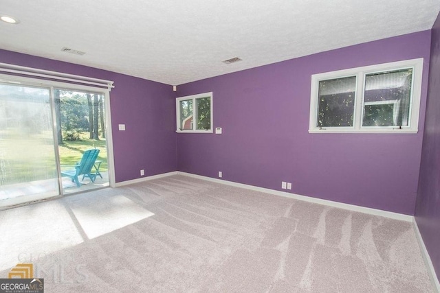 carpeted spare room featuring baseboards, visible vents, and a textured ceiling