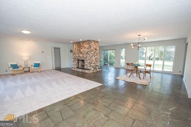 unfurnished living room with an inviting chandelier, stone tile floors, baseboards, and a textured ceiling