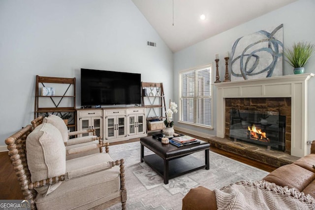 living room with a stone fireplace, high vaulted ceiling, and light hardwood / wood-style flooring