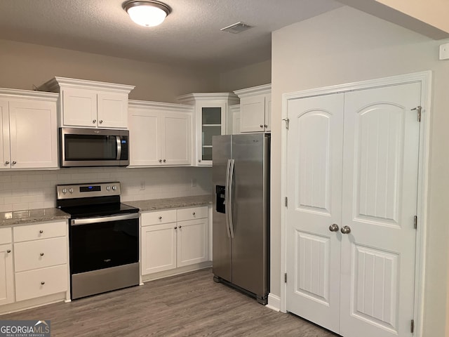 270 Bridgewater Ln SE, Darien, GA 31305 - kitchen with appliances with stainless steel finishes, decorative backsplash, white cabinets, light wood-type flooring, and glass insert cabinets