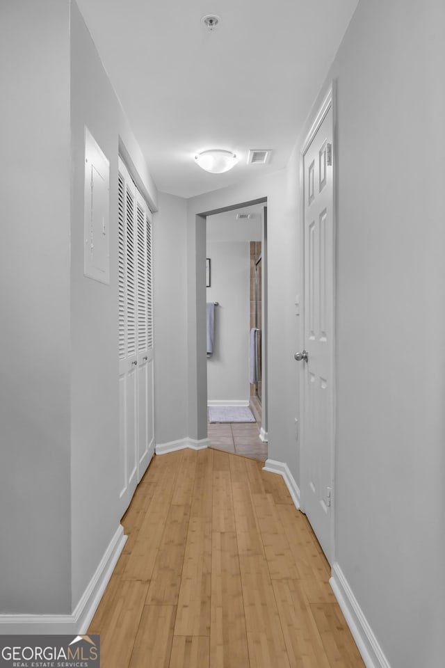 hall with light wood finished floors, baseboards, electric panel, and visible vents