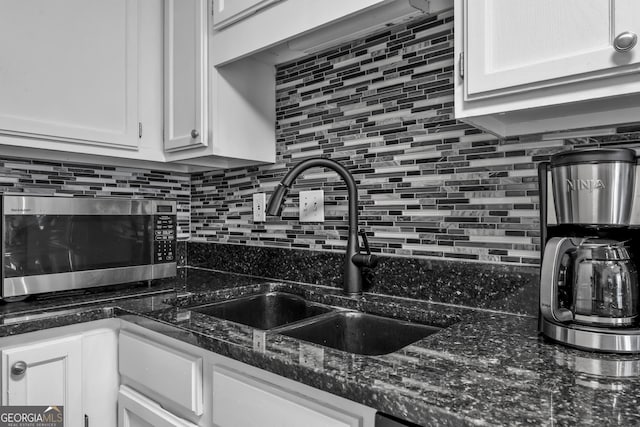 kitchen featuring tasteful backsplash, stainless steel microwave, a sink, and white cabinetry