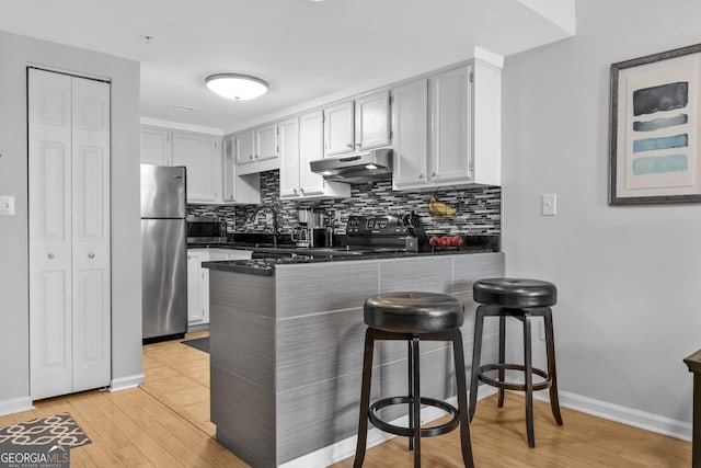 kitchen with dark countertops, backsplash, appliances with stainless steel finishes, a peninsula, and under cabinet range hood