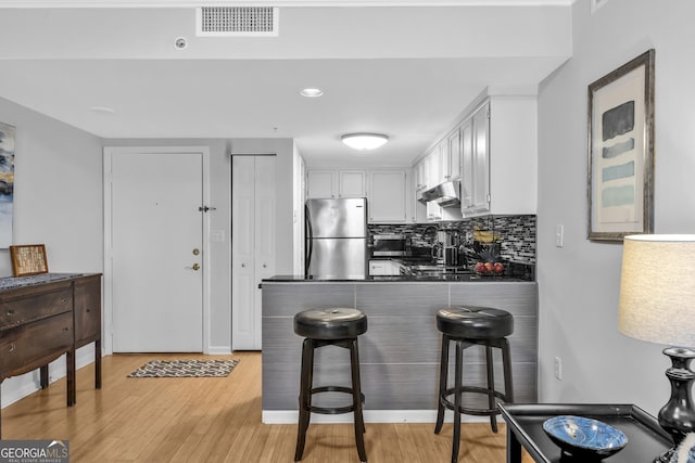 kitchen with a peninsula, visible vents, freestanding refrigerator, tasteful backsplash, and dark countertops