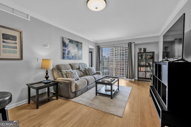 living room featuring ornamental molding, light wood-type flooring, visible vents, and baseboards