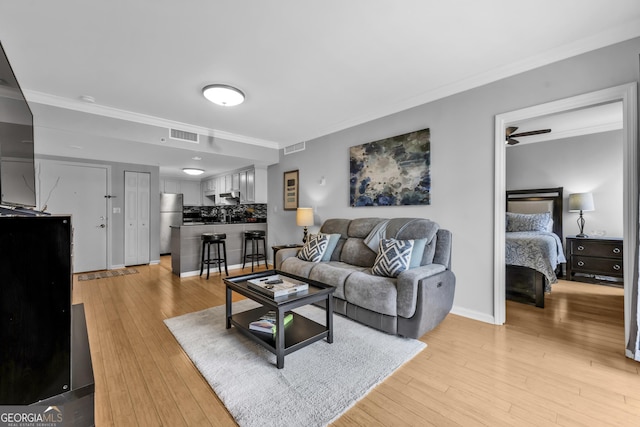 living room featuring ornamental molding, light wood-type flooring, visible vents, and baseboards