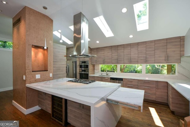 kitchen featuring island exhaust hood, light stone counters, kitchen peninsula, stainless steel appliances, and a healthy amount of sunlight