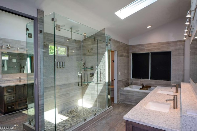 bathroom featuring hardwood / wood-style flooring, vanity, vaulted ceiling with skylight, and separate shower and tub