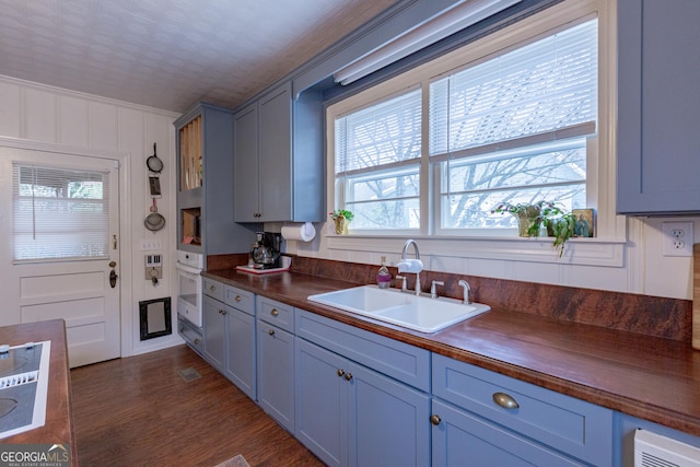 kitchen featuring dark wood-type flooring, sink, ornamental molding, gray cabinets, and oven