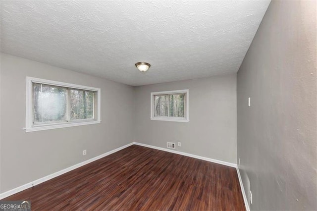 unfurnished room featuring a wealth of natural light, a textured ceiling, and dark hardwood / wood-style floors