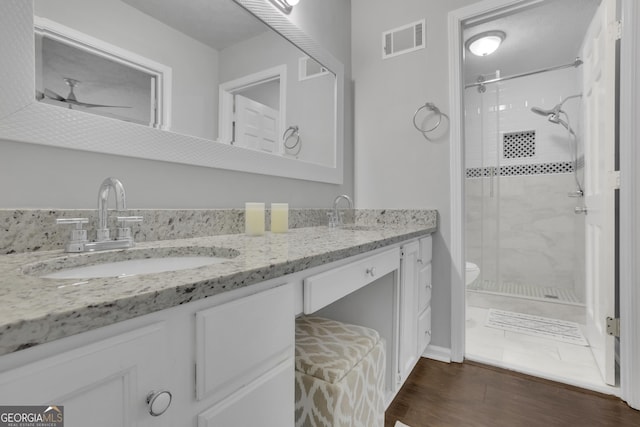 bathroom featuring wood-type flooring, vanity, walk in shower, ceiling fan, and toilet