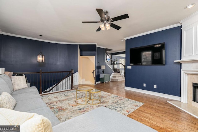 living room featuring a fireplace, crown molding, wood-type flooring, and ceiling fan