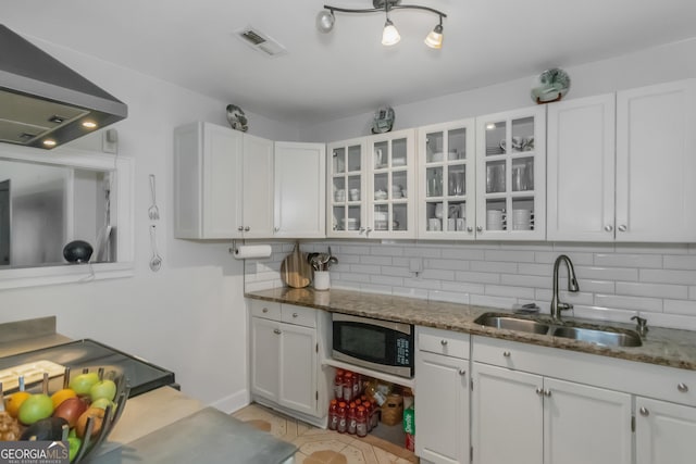 kitchen featuring sink, wall chimney range hood, stainless steel microwave, white cabinets, and dark stone counters