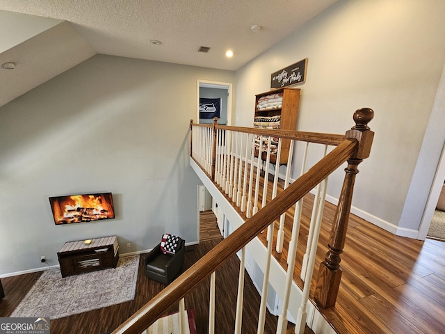 stairway with hardwood / wood-style flooring, vaulted ceiling, and a textured ceiling