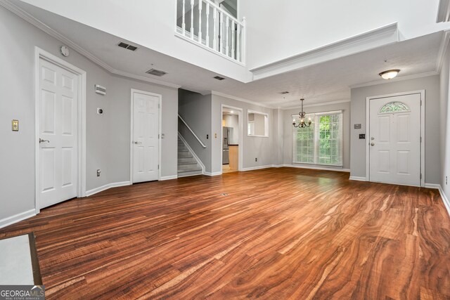 unfurnished living room with stairs, dark wood-type flooring, visible vents, crown molding, and an inviting chandelier