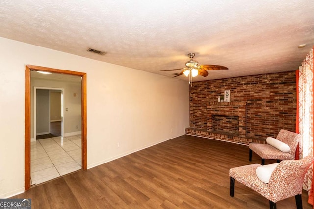 unfurnished room featuring ceiling fan, wood-type flooring, a textured ceiling, brick wall, and a brick fireplace