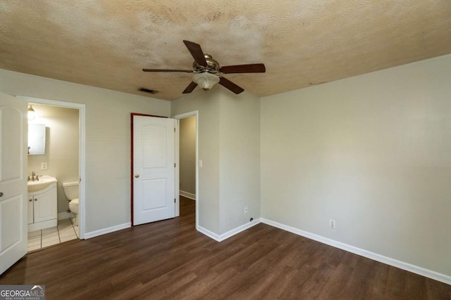 unfurnished bedroom featuring dark wood-type flooring, a textured ceiling, and ensuite bath