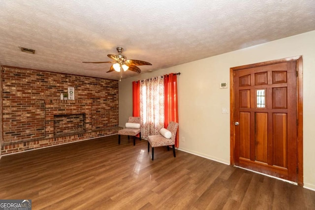 unfurnished room featuring ceiling fan, dark wood-type flooring, a textured ceiling, and brick wall