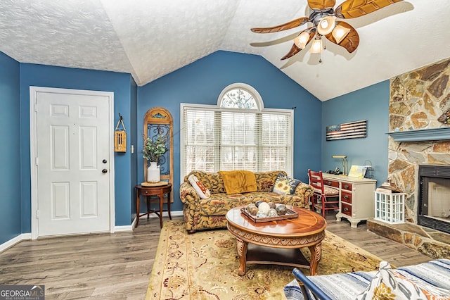 living room featuring a fireplace, lofted ceiling, hardwood / wood-style flooring, ceiling fan, and a textured ceiling