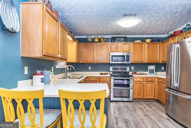 kitchen featuring sink, crown molding, stainless steel appliances, a textured ceiling, and light wood-type flooring