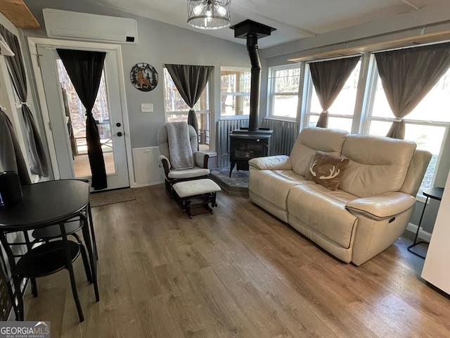 living room with wood-type flooring, lofted ceiling, a wood stove, and a wall unit AC