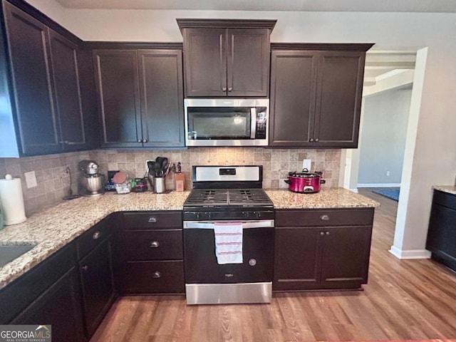 kitchen featuring baseboards, light wood finished floors, stainless steel appliances, decorative backsplash, and dark brown cabinetry