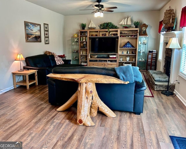 living area with baseboards, a fireplace, wood finished floors, and a ceiling fan