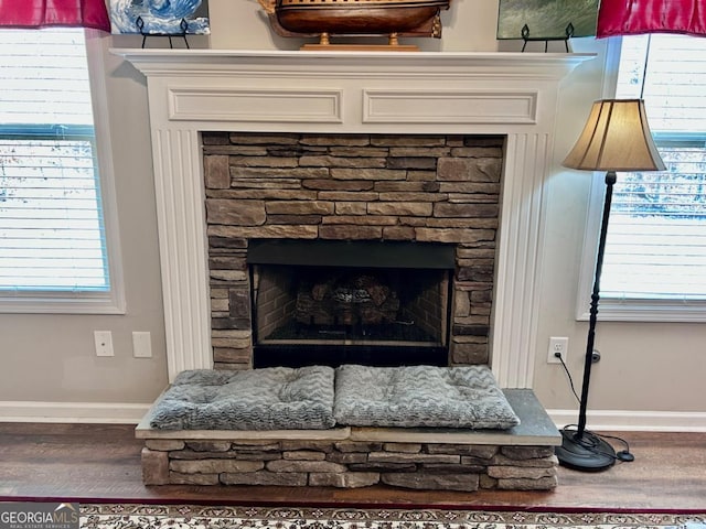 interior details featuring baseboards, a stone fireplace, and wood finished floors