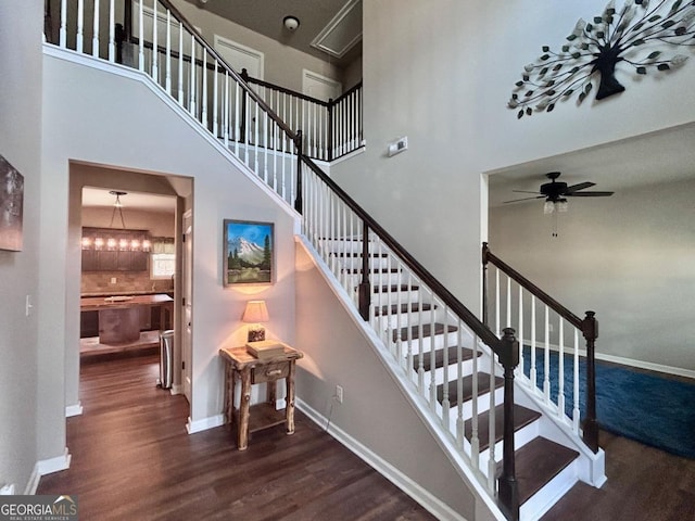 staircase with wood finished floors, baseboards, and a towering ceiling