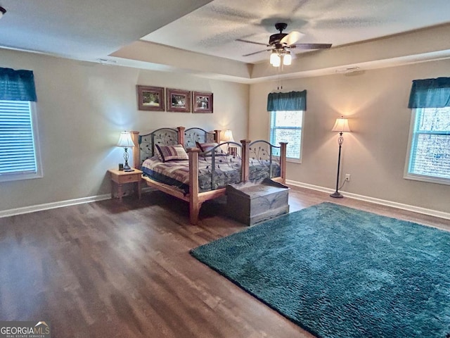 bedroom featuring a raised ceiling, wood finished floors, baseboards, and ceiling fan