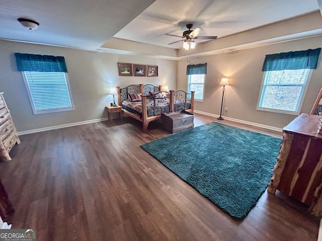 bedroom with a tray ceiling, baseboards, wood finished floors, and a ceiling fan