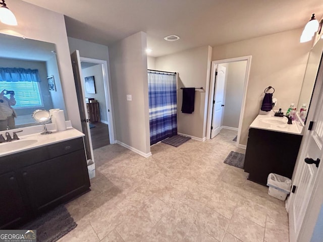 full bath featuring curtained shower, two vanities, baseboards, and a sink