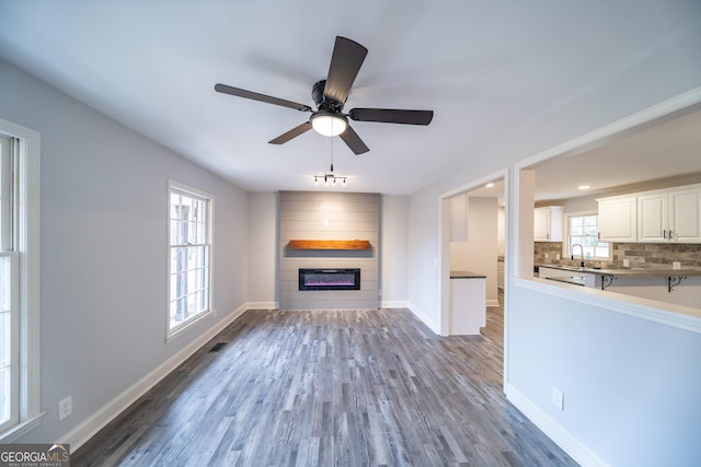 unfurnished living room featuring dark hardwood / wood-style flooring, sink, a large fireplace, and ceiling fan