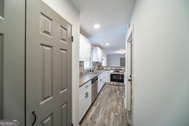 kitchen featuring sink, appliances with stainless steel finishes, white cabinets, decorative backsplash, and light wood-type flooring