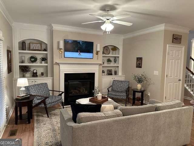 living room featuring crown molding, dark wood-type flooring, ceiling fan, and built in shelves